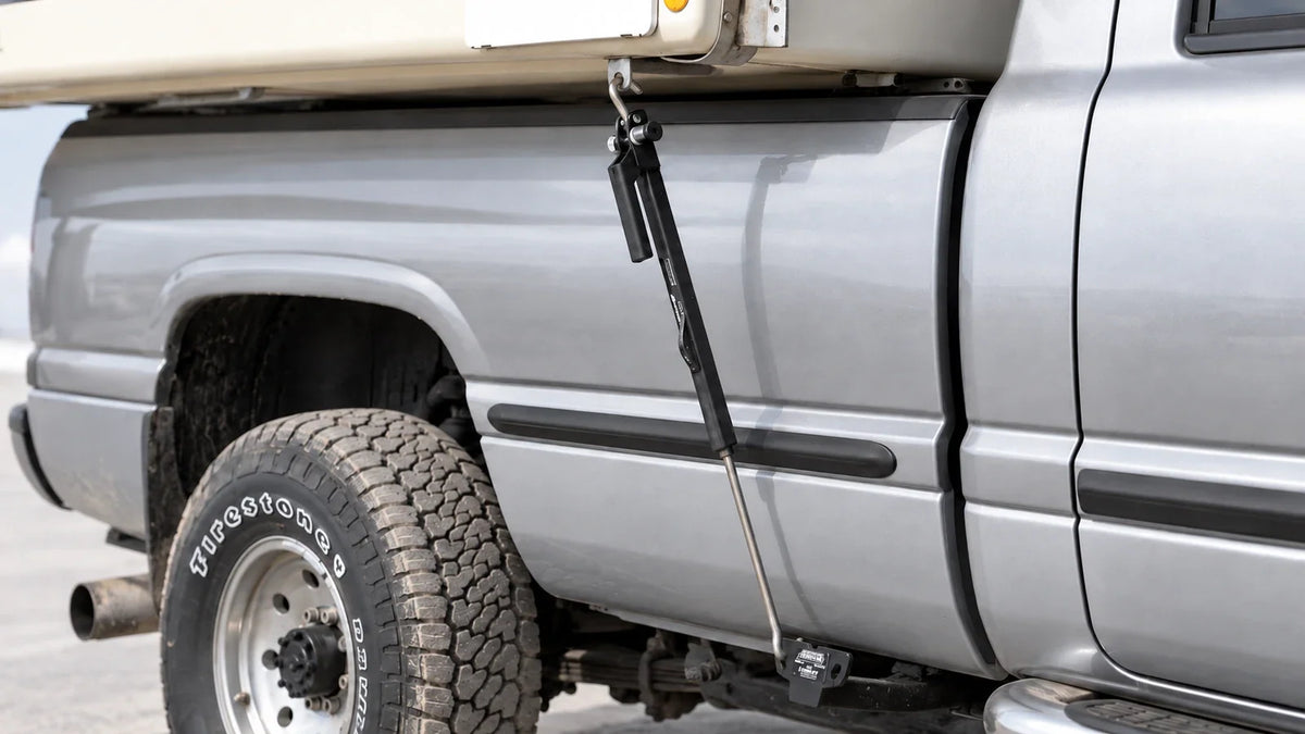 Black TorkLift FastGun turnbuckle connecting a camper anchor to the truck-side tie-down insert beside a silver pickup bed.