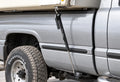 Black TorkLift FastGun turnbuckle connecting a camper anchor to the truck-side tie-down insert beside a silver pickup bed.