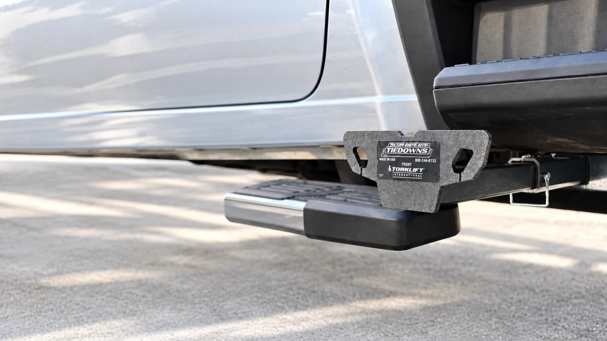 Close-up of an installed TorkLift C2225 camper tie-down insert, receiver and retaining pin beneath a silver pickup.